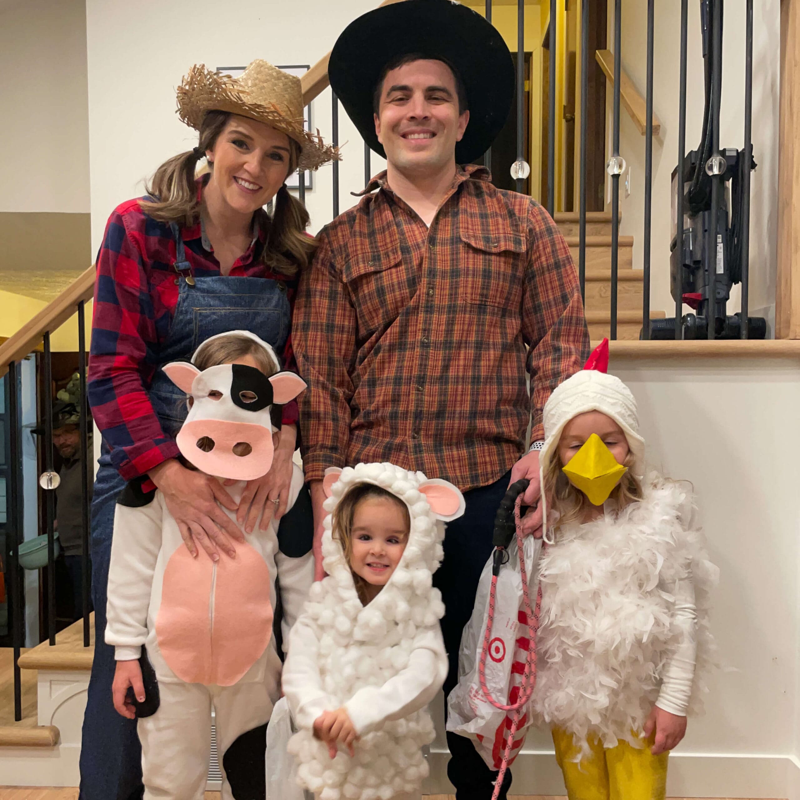 Family in easy DIY Halloween costumes with farm theme — mom and dad as farmers, kids as a cow, sheep, and chicken in homemade no-sew outfits.