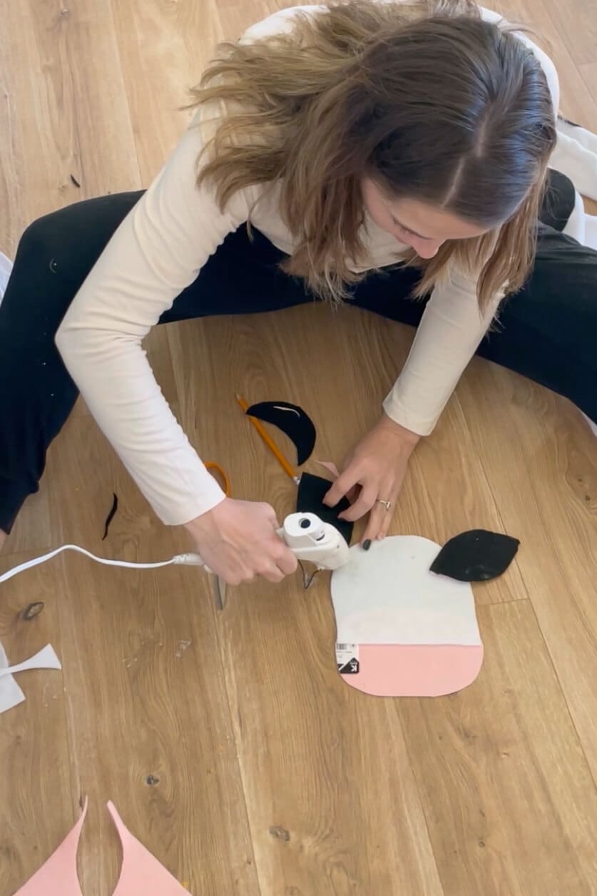 Gluing black felt cow ears onto a white and pink mask for a DIY cow costume.