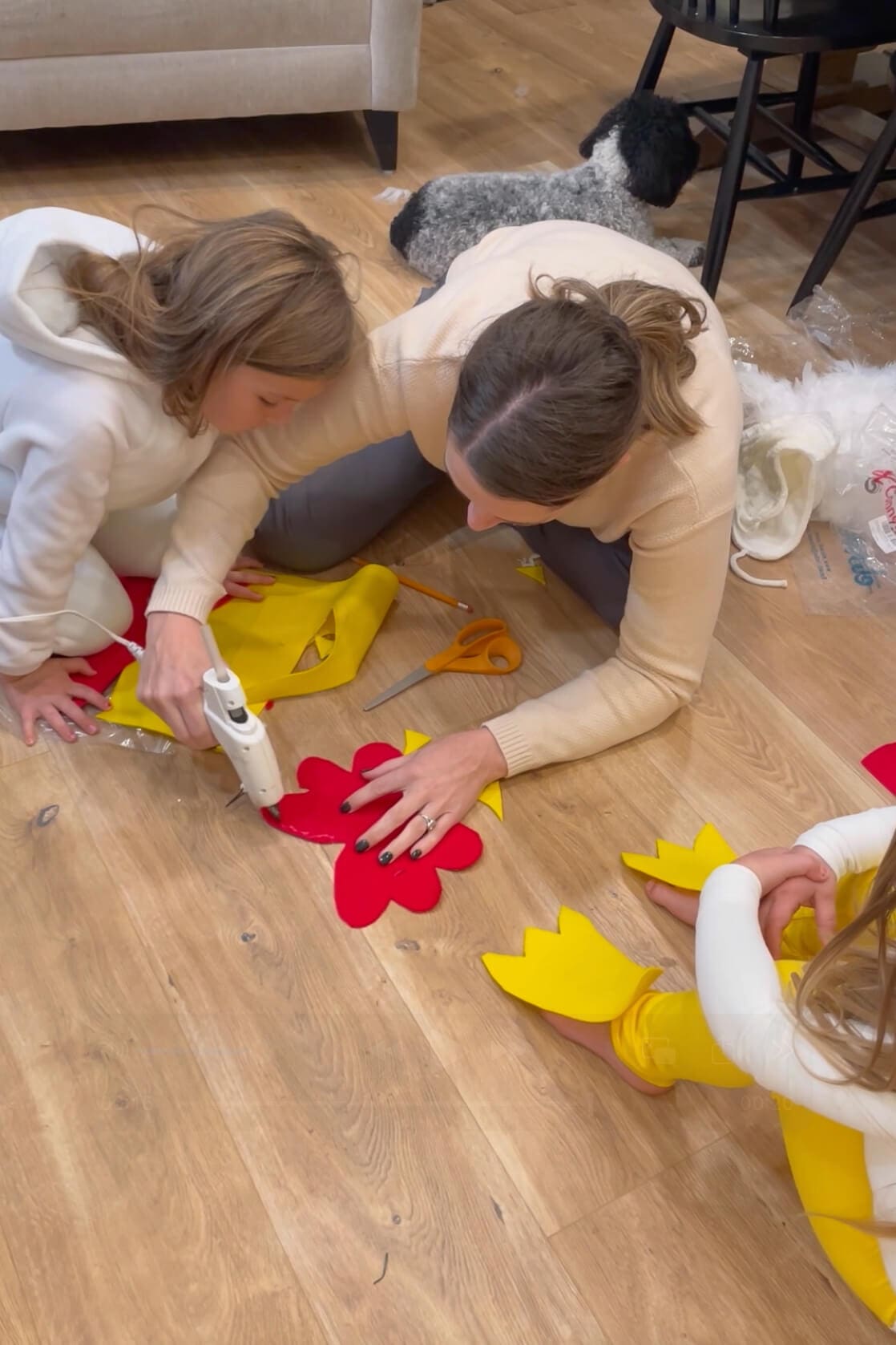 Mom and children using a hot glue gun to assemble red felt chicken combs and yellow felt feet for a homemade costume.