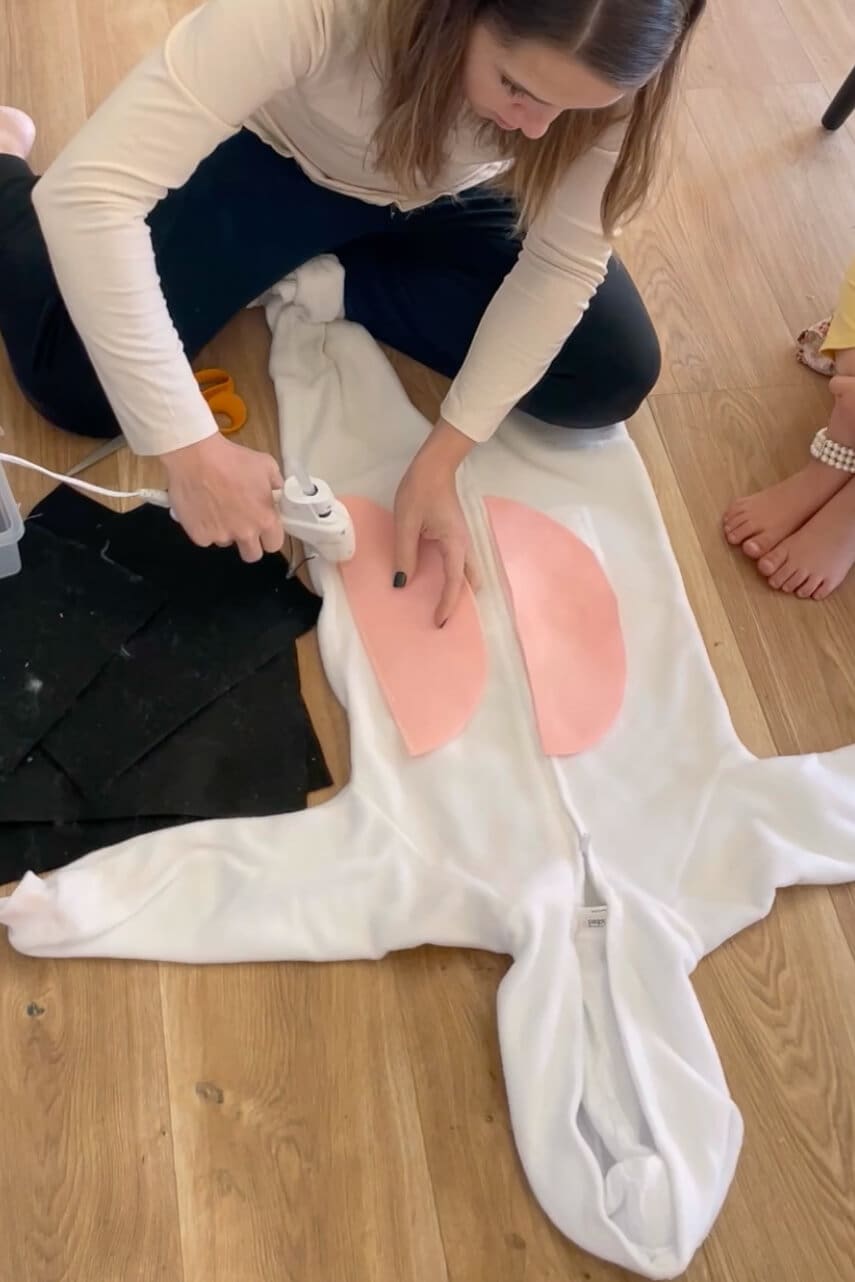 Gluing pink felt belly patches onto a white jumpsuit while making a DIY cow costume for a child's Halloween costume.