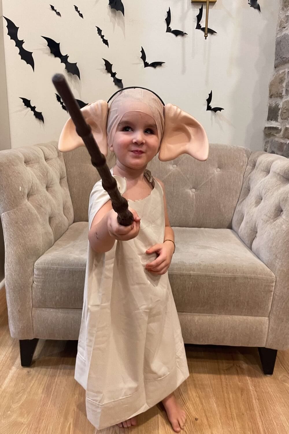 Child in a DIY Harry Potter costume dressed as Dobby the house elf holding a wand for Halloween.
