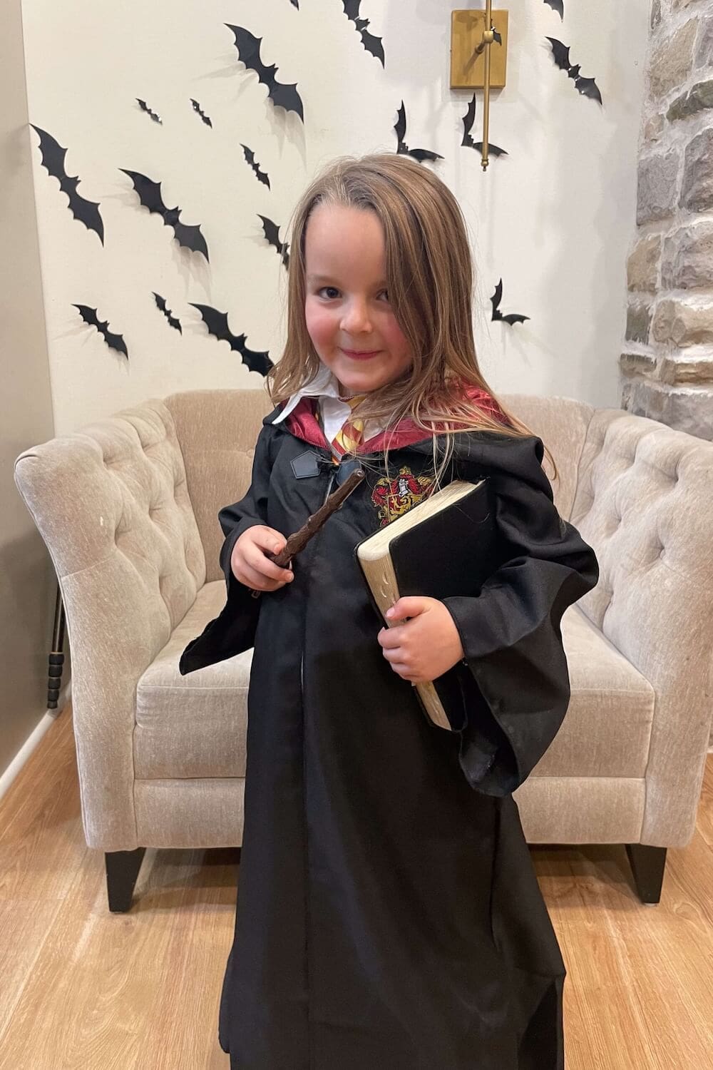 Child dressed as Hermione Granger with Gryffindor robe, wand, and spellbook.