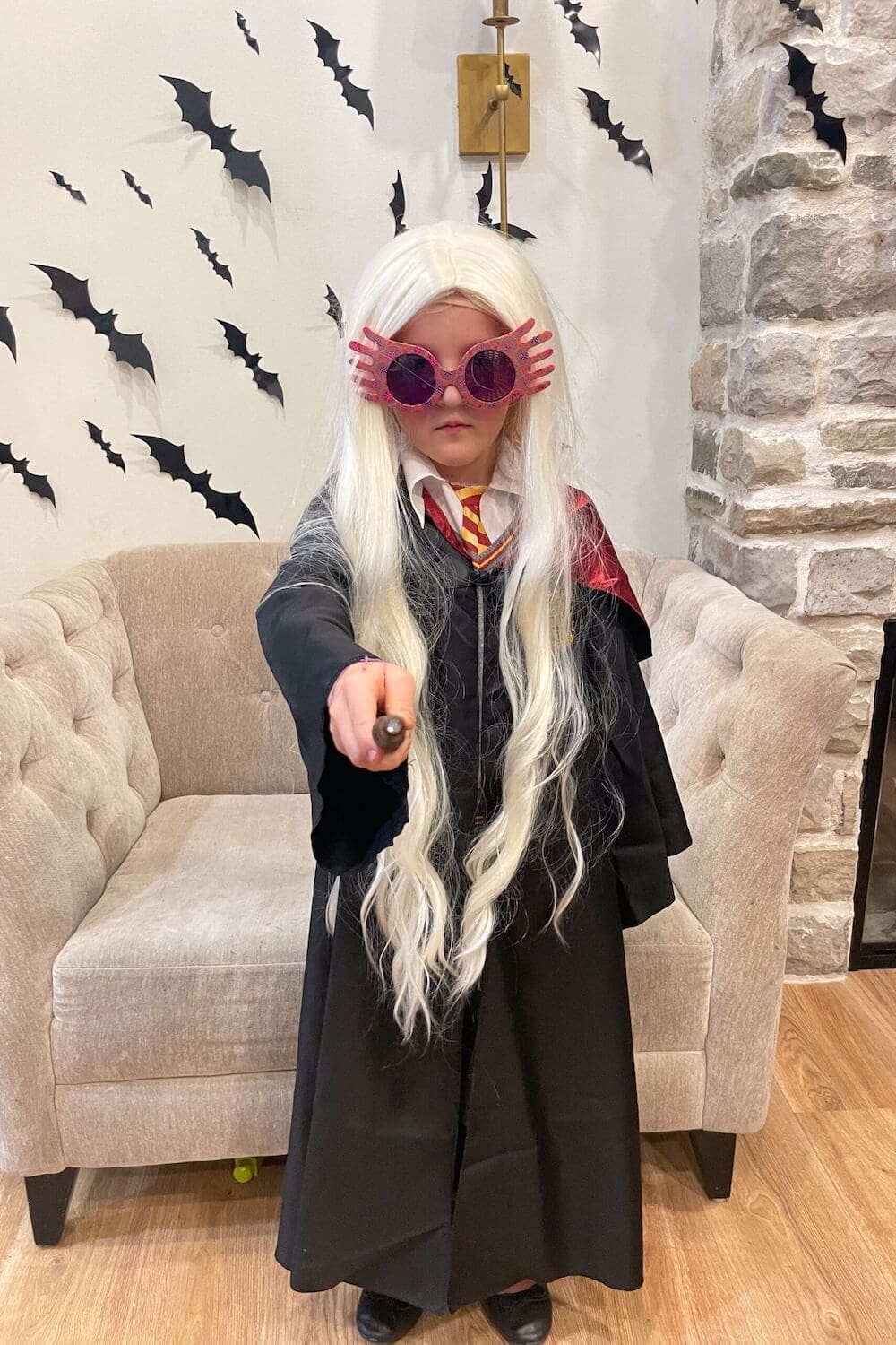 Child in Harry Potter family costume dressed as Luna Lovegood with Spectrespecs glasses, long blonde wig, and wand.