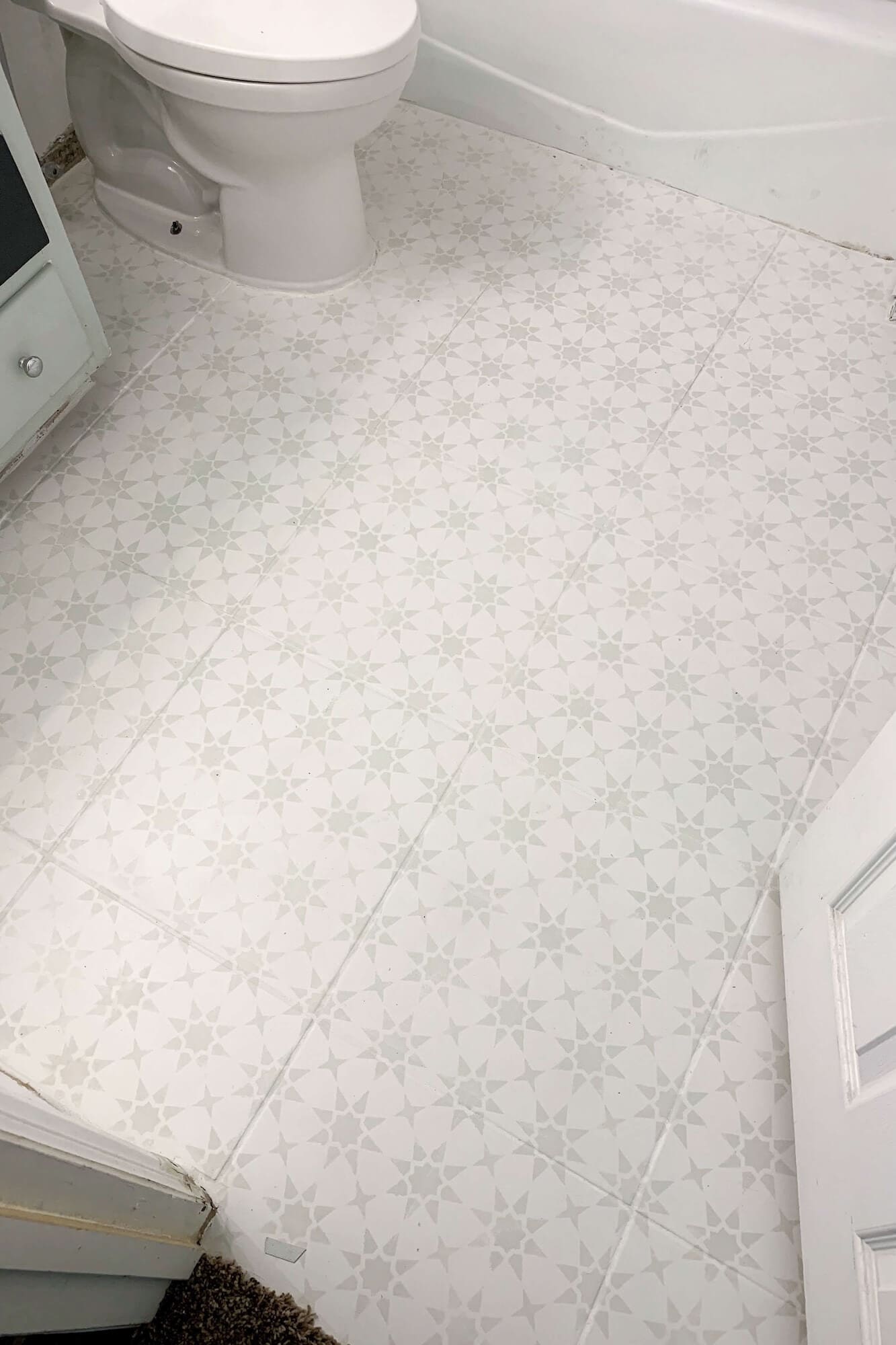 Overhead view of small bathroom floor makeover showing painted and stenciled tiles from doorway to tub.