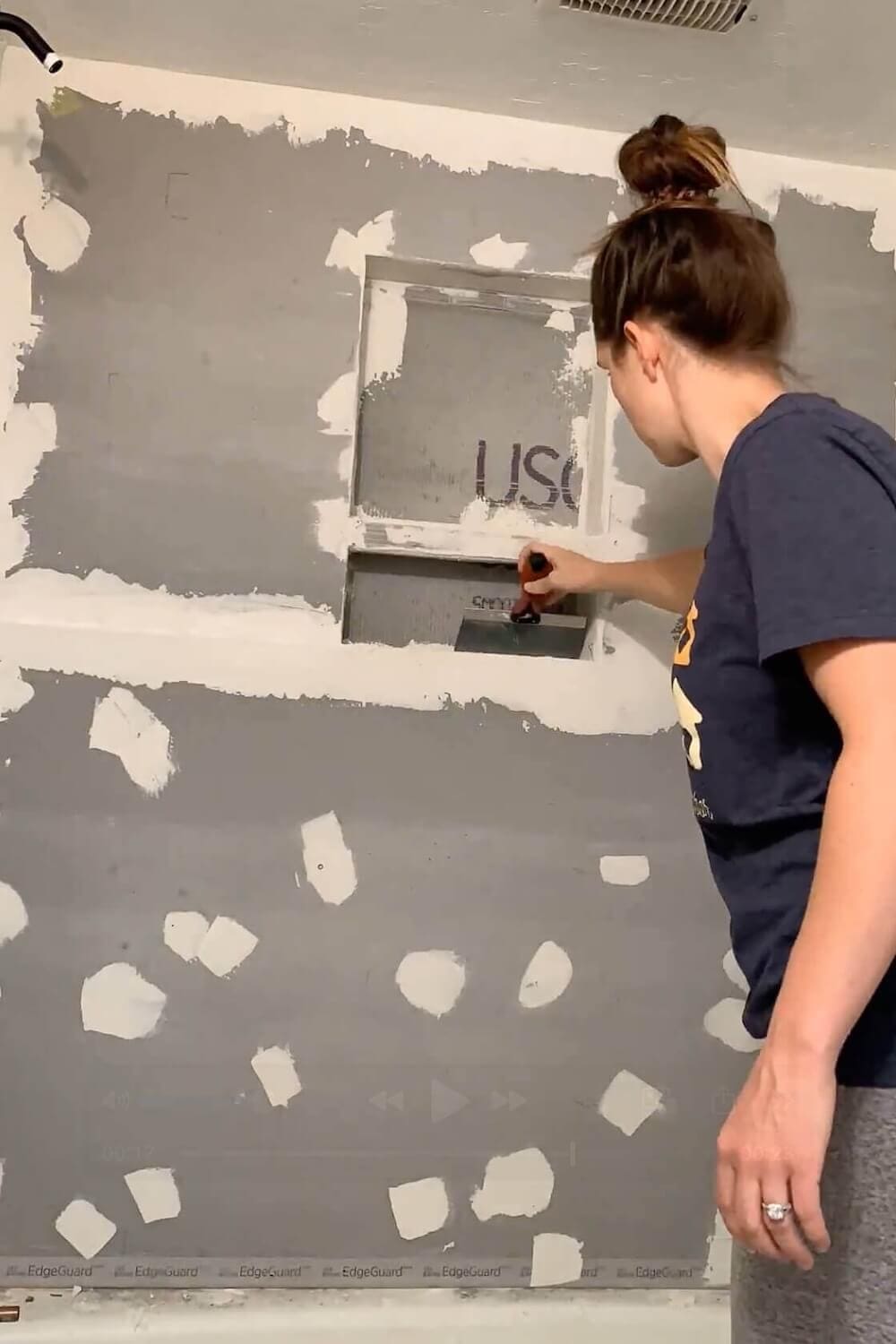 Applying mesh tape and thinset to the joints around a shower niche to prepare it for waterproofing.