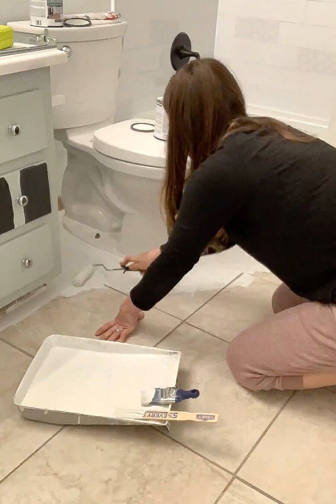 Rolling white bonding primer over beige bathroom floor tiles next to the tub and toilet.