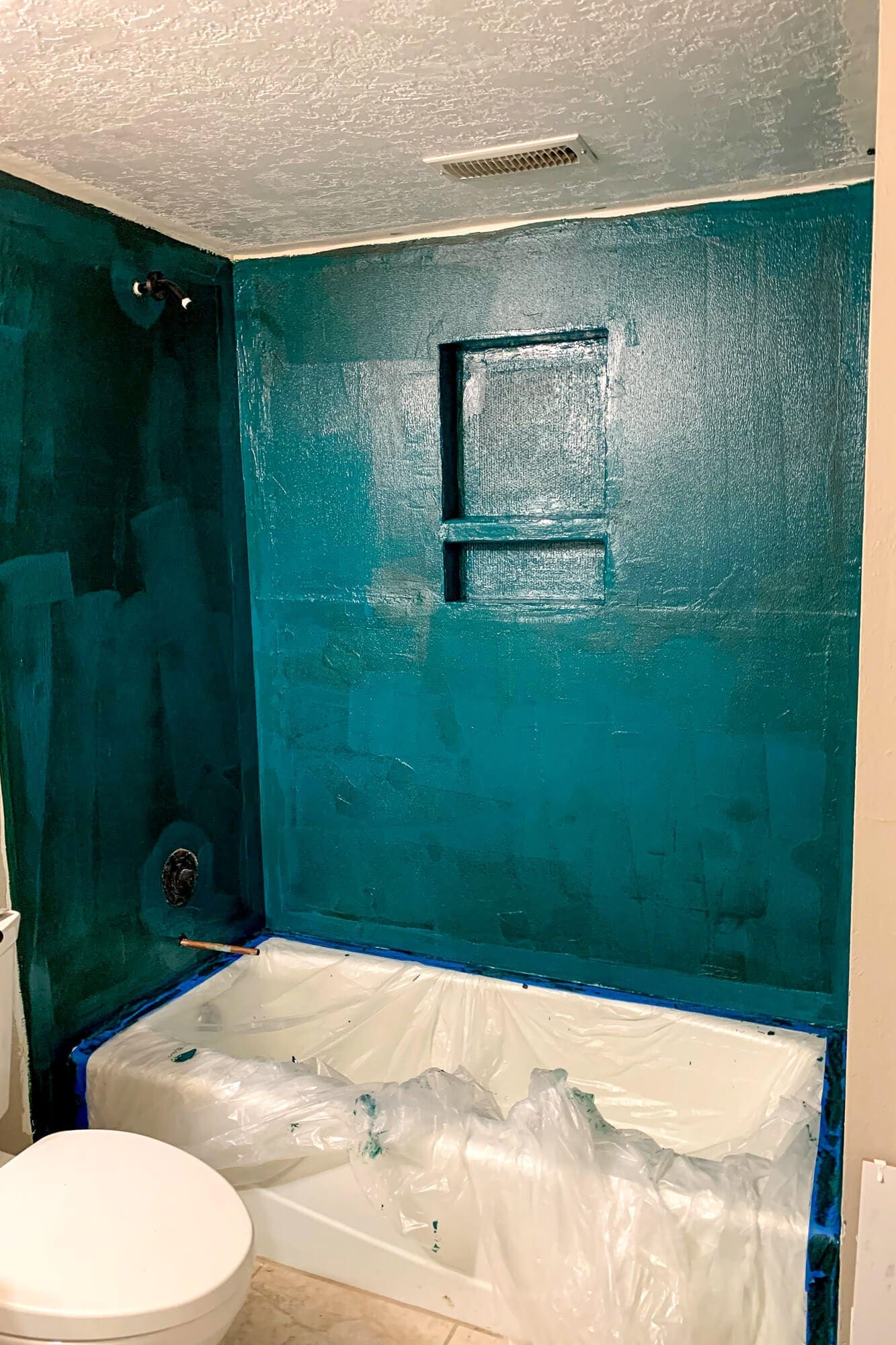 Applying the first coat of waterproofing membrane to shower walls during basement bathroom remodel, covering cement board completely.