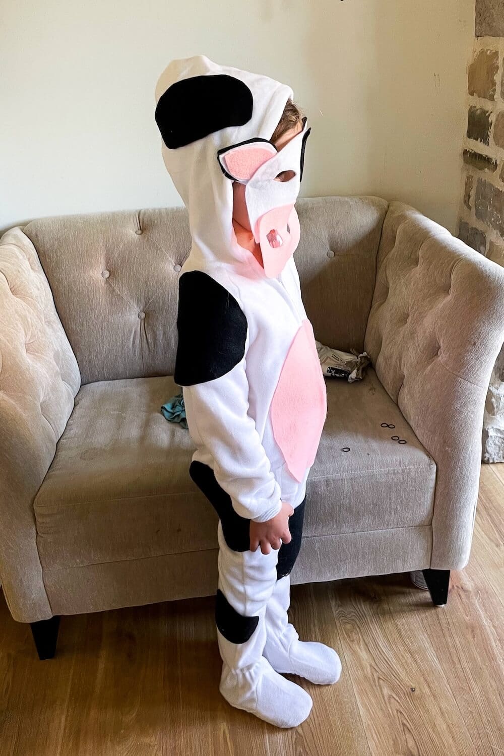 Side view of a child in a DIY cow costume with black spots, pink snout, and hood.