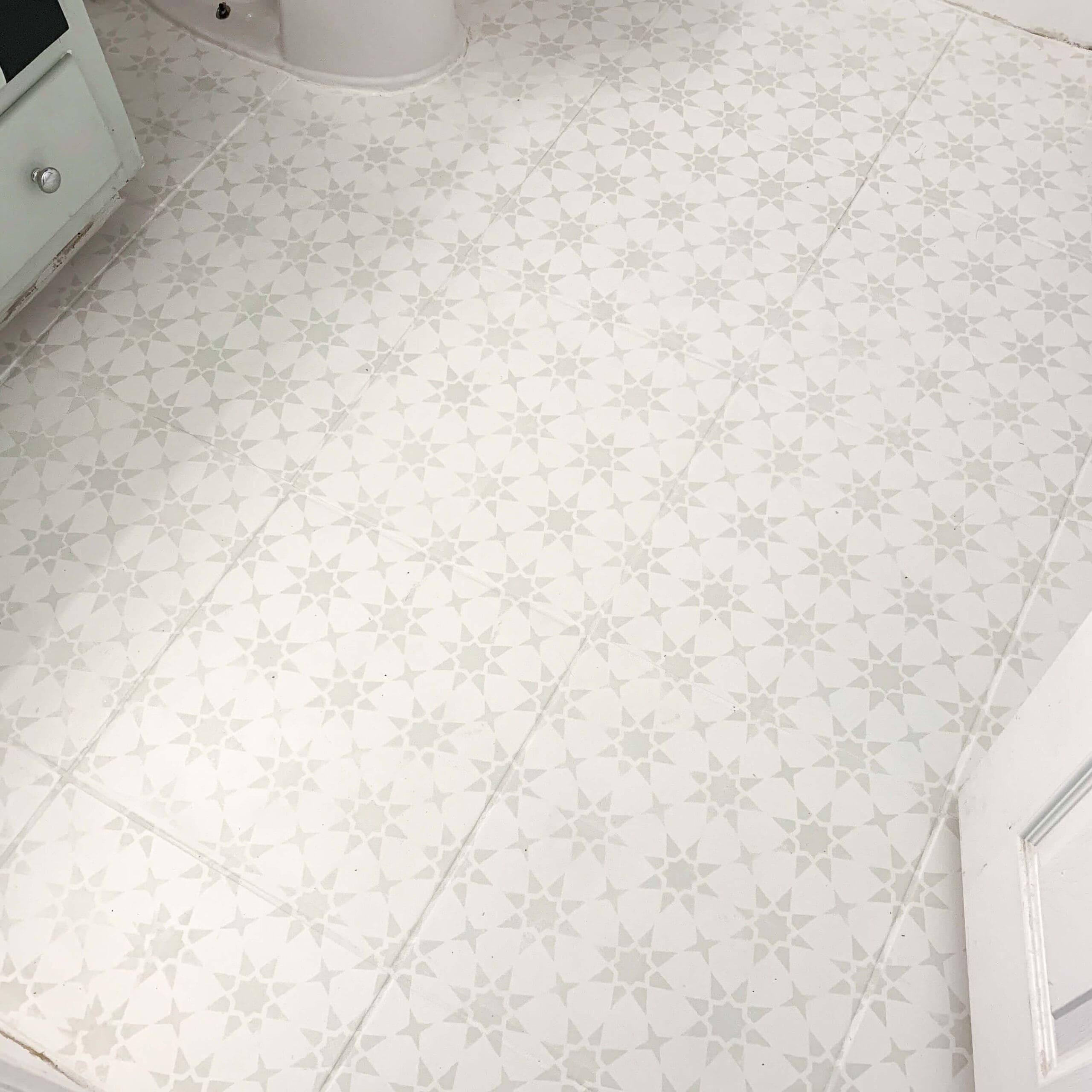 Detailed close-up of the stenciled star pattern painted over square bathroom tiles, showing the light gray design on a cream background near the base of the toilet and vanity.