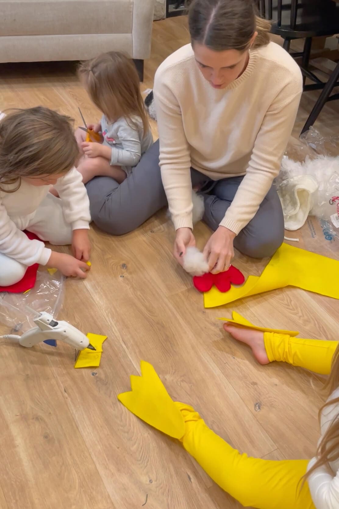 Mom stuffing a red felt chicken comb with batting while children work on yellow felt feet pieces for a handmade costume.
