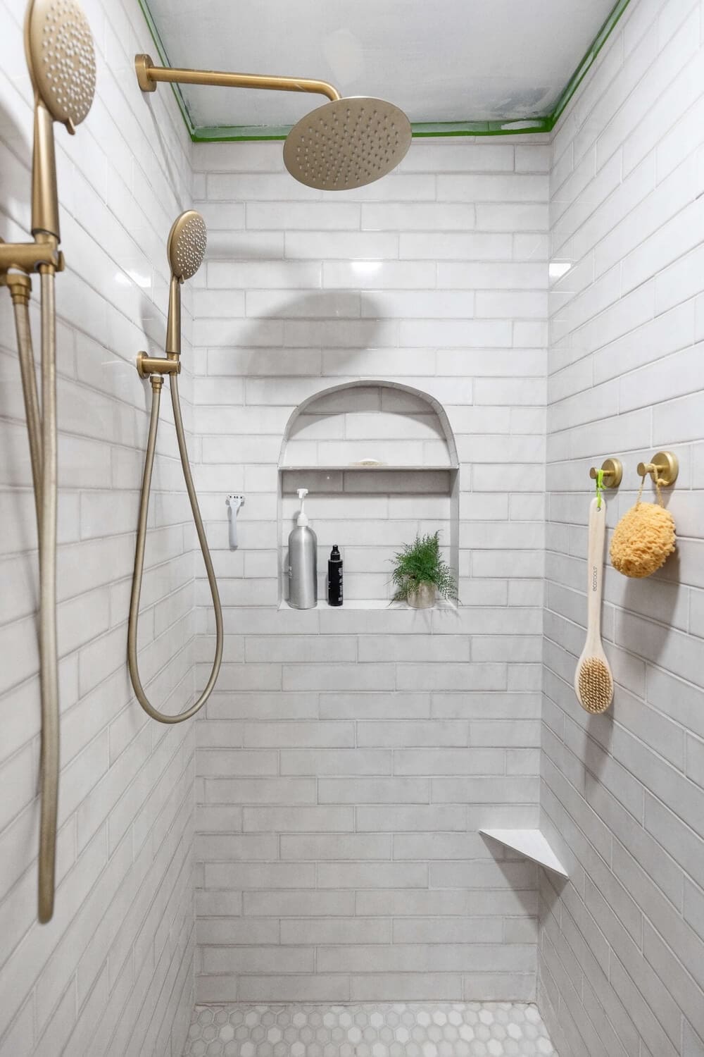 Walk-in shower with gold fixtures, arched shower niche, and light gray wall tile for a modern, elevated bathroom look.