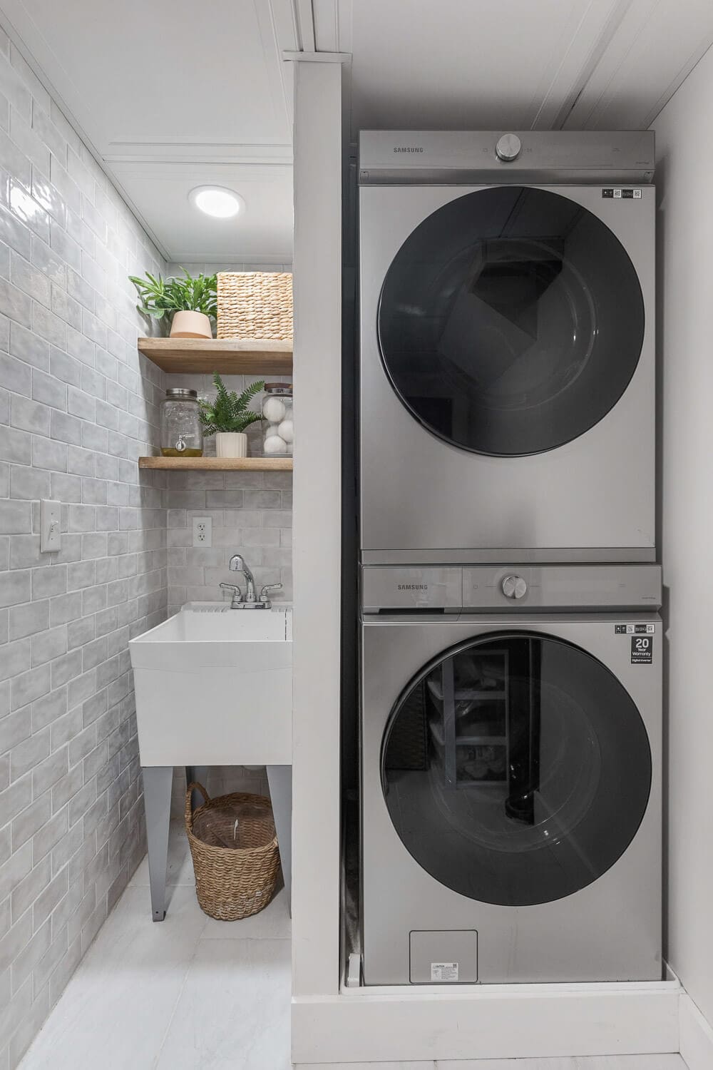 Basement laundry remodel with stacked washer and dryer, subway tile, and wood shelves.