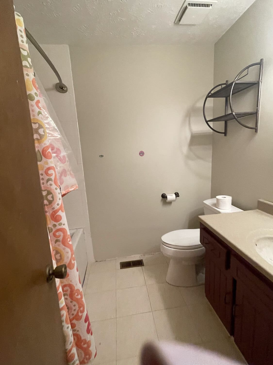 Outdated bathroom before remodel with beige tile, dated vanity, and shower curtain.