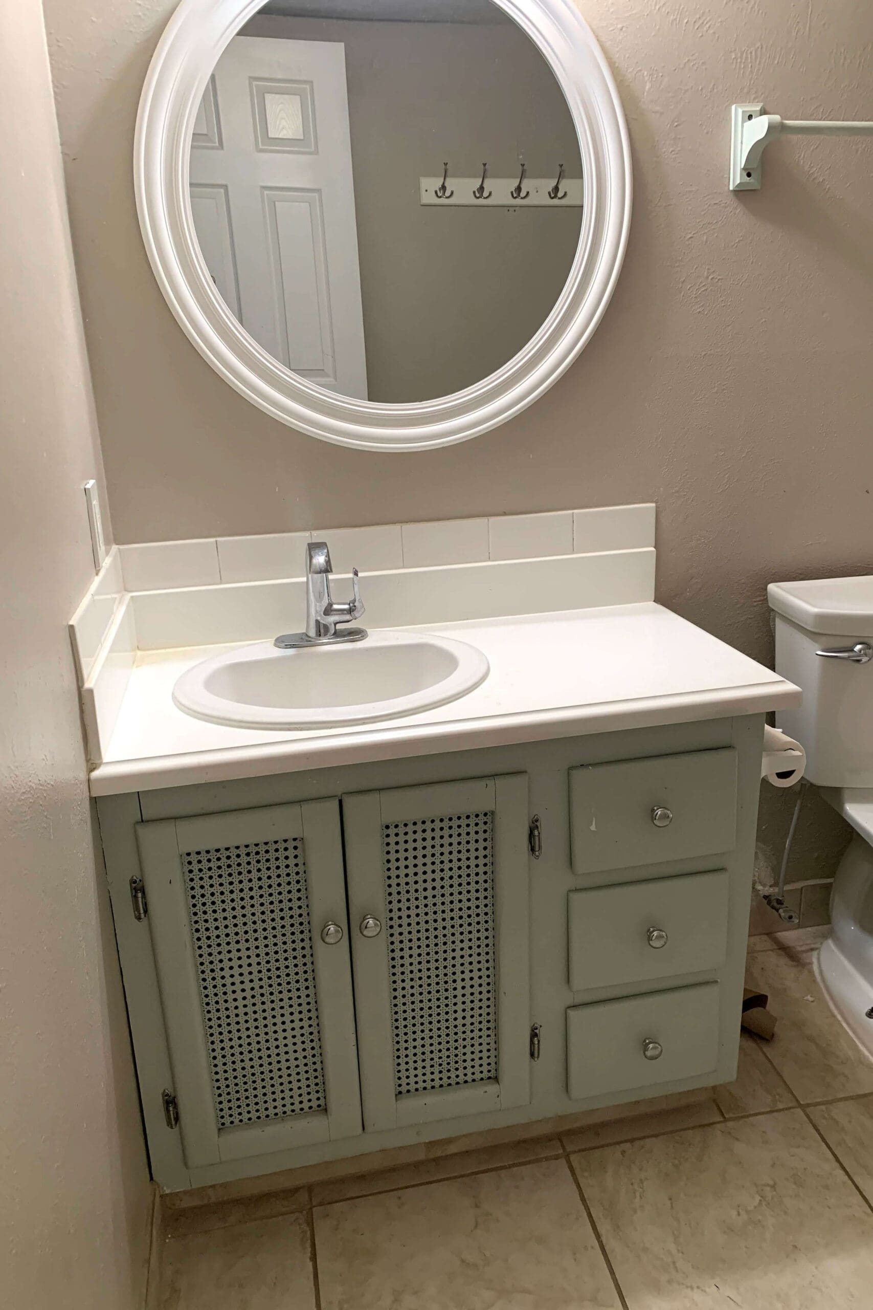 Close-up of worn green bathroom cabinet with scuffed finish and dated knobs before painting.