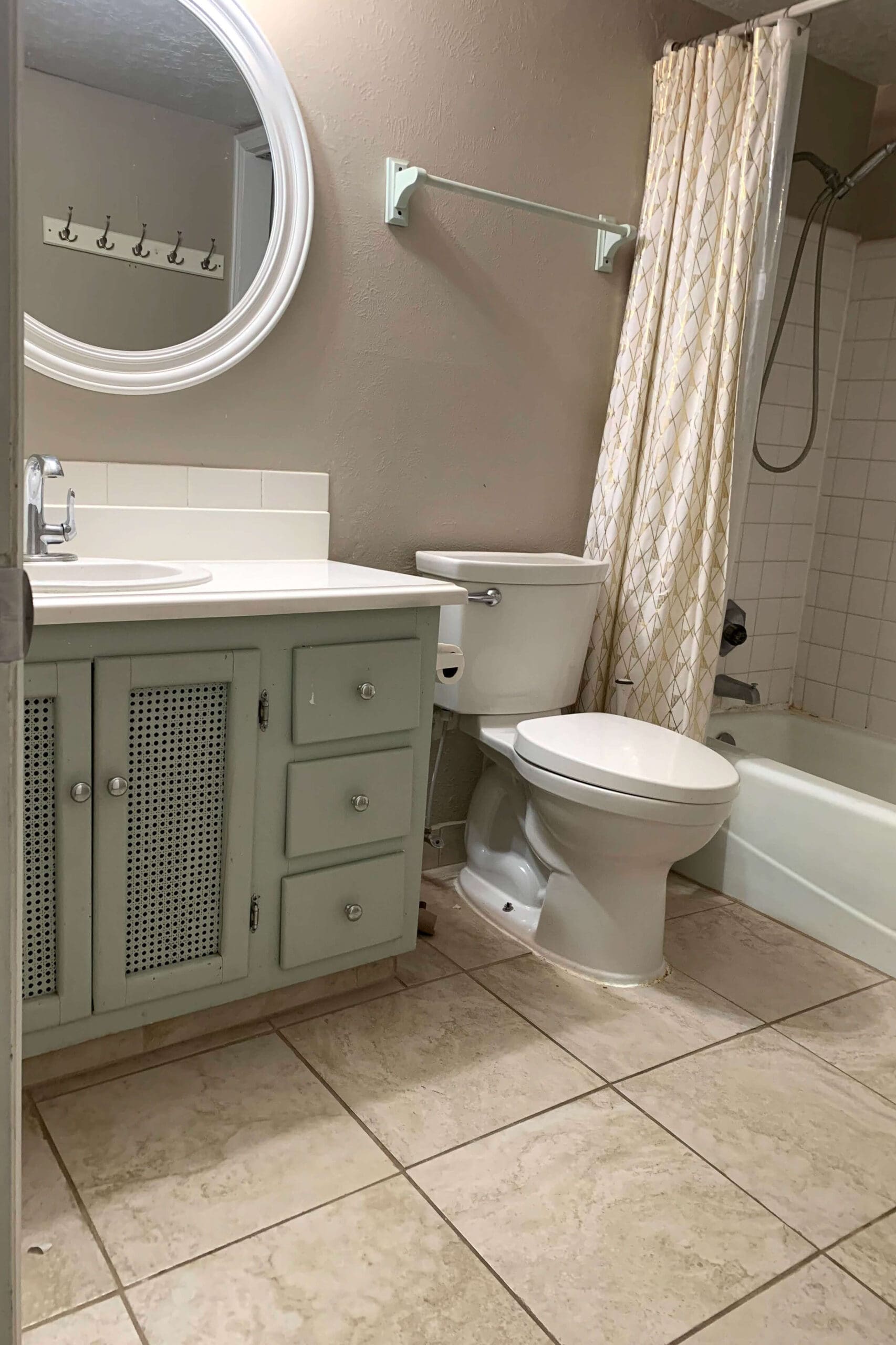 Outdated bathroom vanity and plain mirror with chipped green doors, mismatched hardware, and beige walls before remodel.