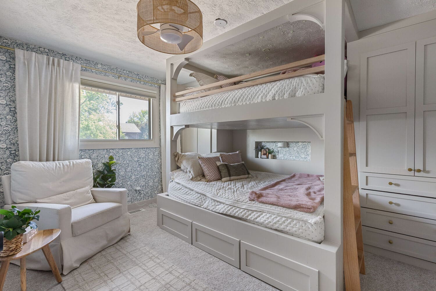 DIY home renovation bedroom with custom white bunk beds, built-in storage, and blue wallpaper.