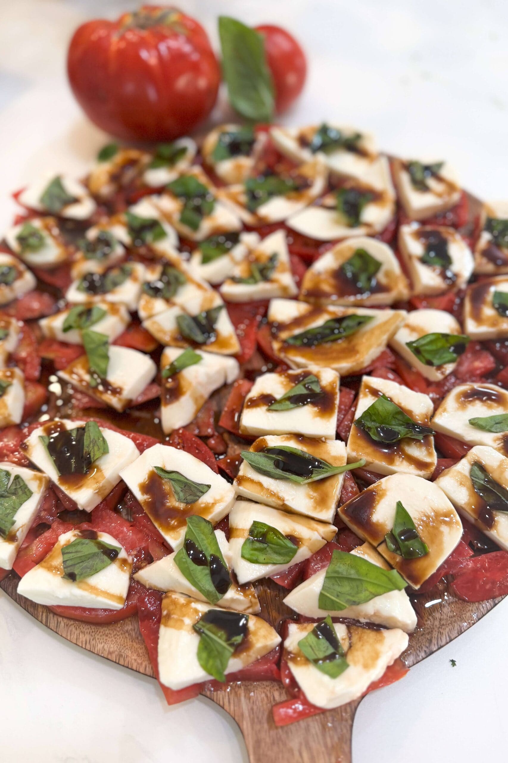 Classic caprese salad with fresh tomato slices, mozzarella, basil leaves, and balsamic glaze drizzled on top, served on a wooden board.