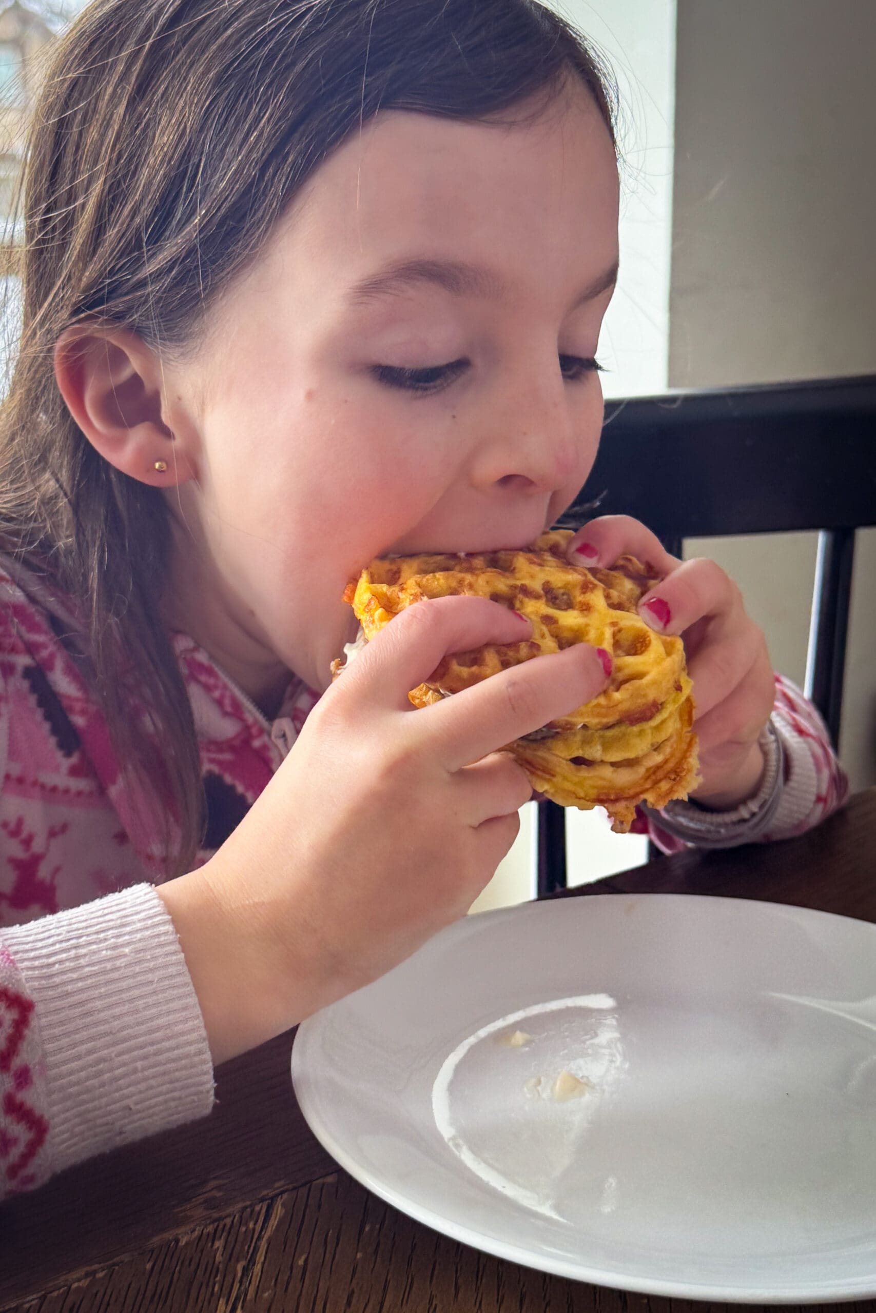 child eating a chaffle sandwich with egg and sausage