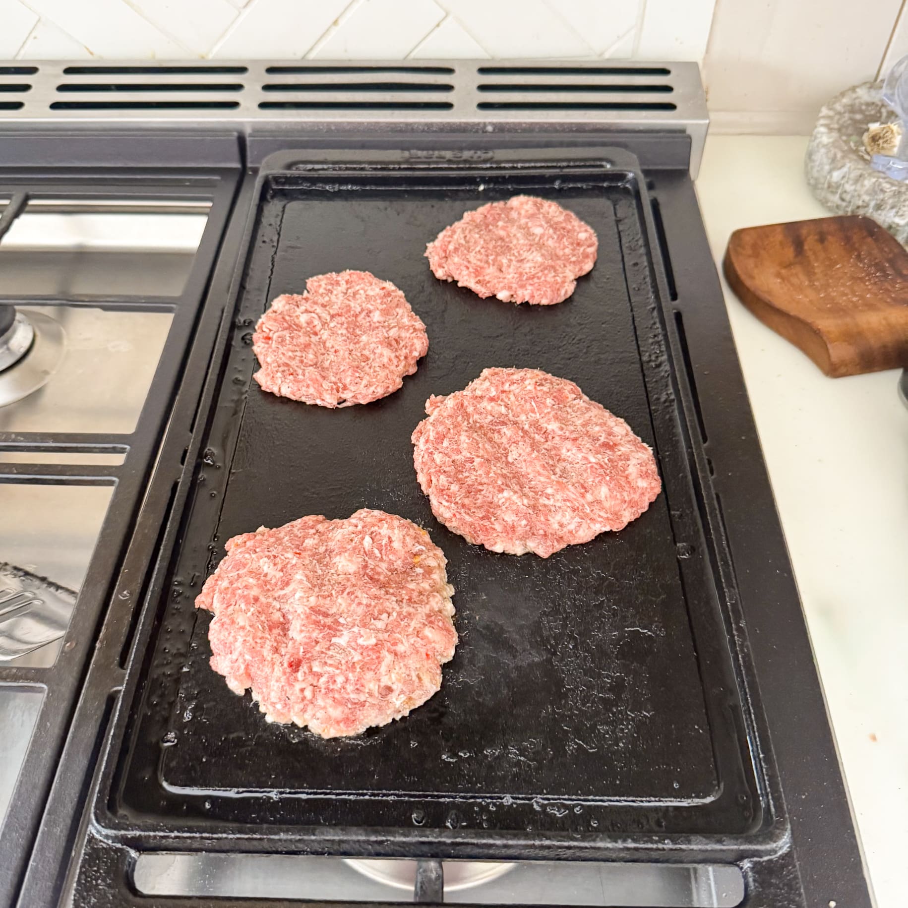 Raw sausage patties cooking on a stovetop griddle for a homemade carnivore breakfast.