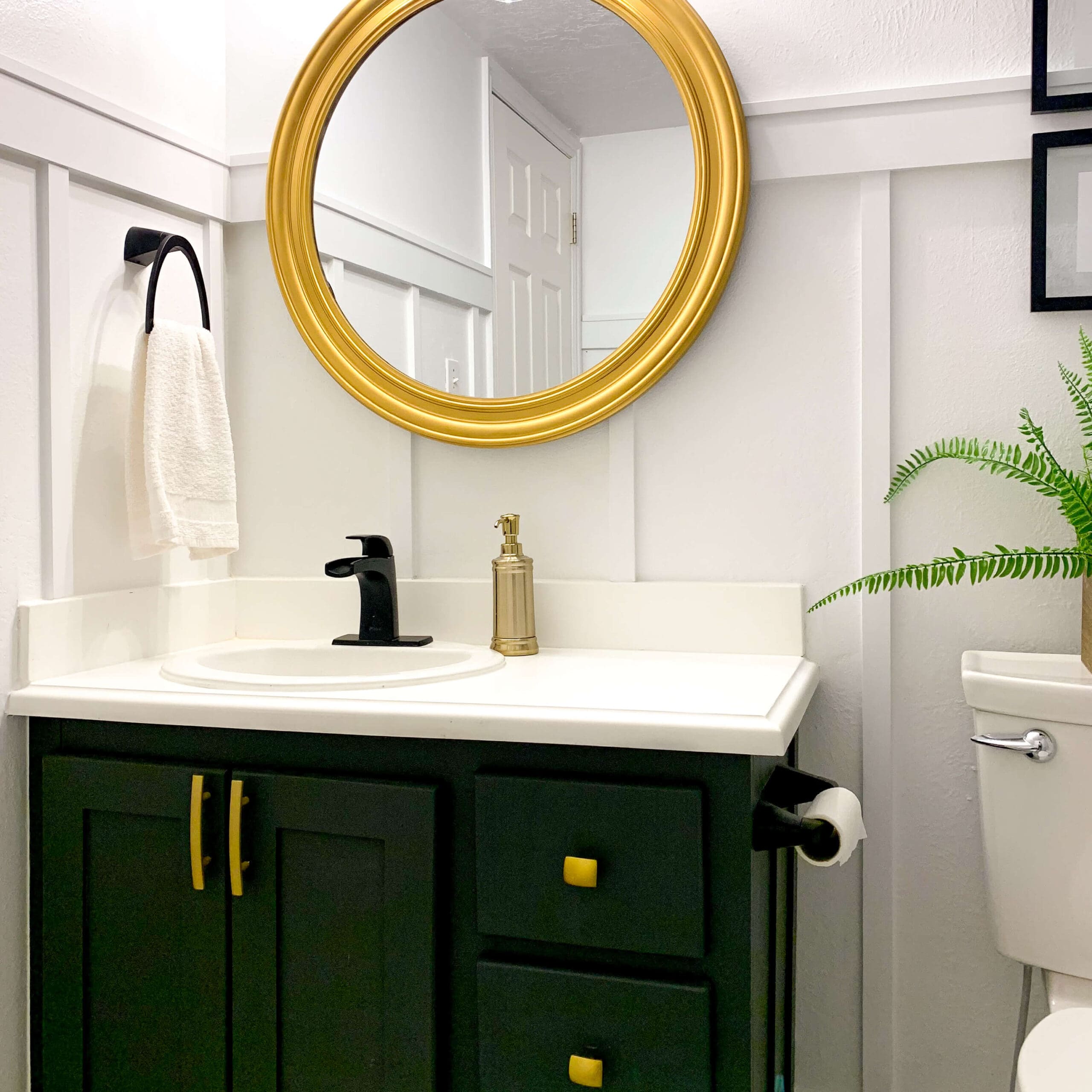 DIY board and batten wall painted white in a bathroom with modern vanity and gold mirror.