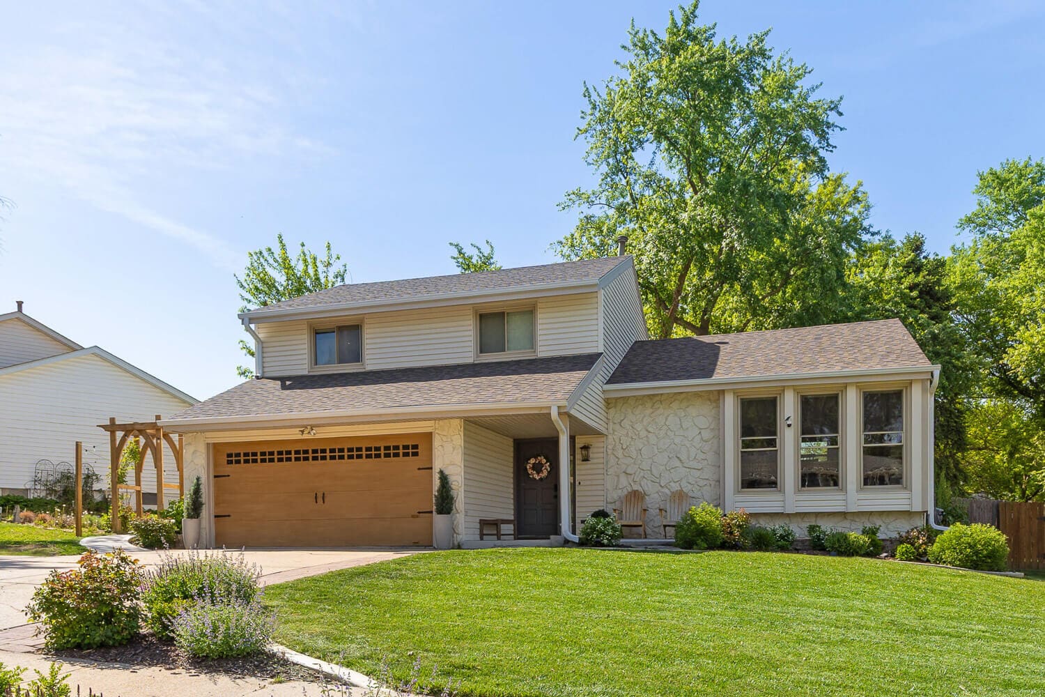 Front exterior after home remodel before and after project with new garage door, stone siding, and landscaping.