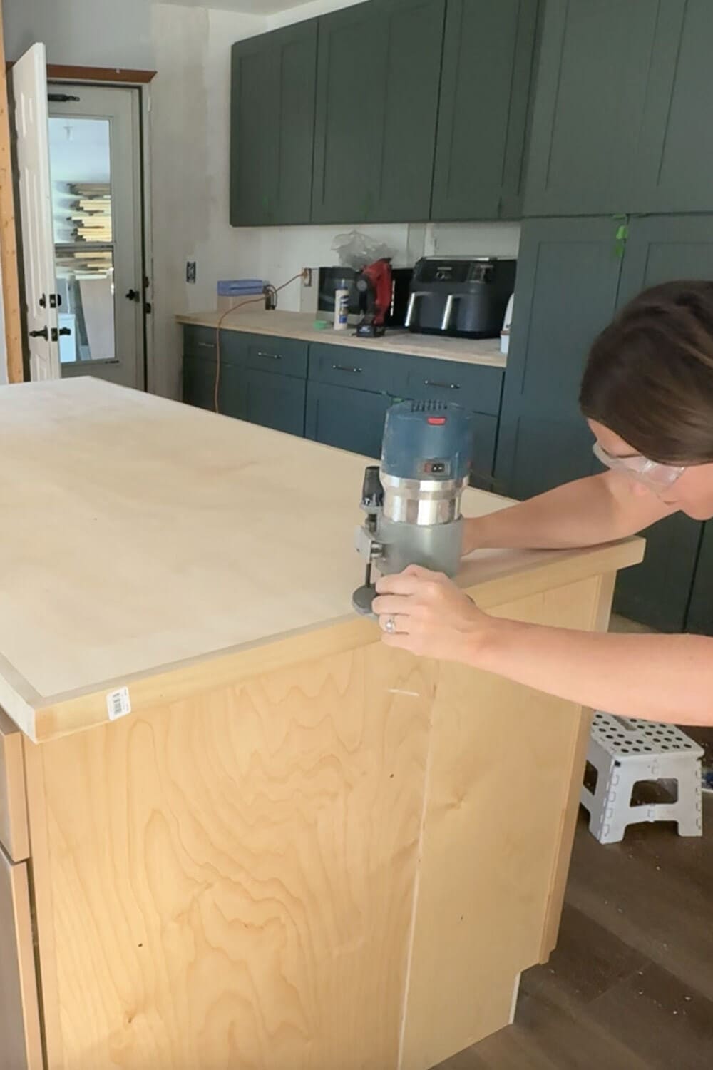 DIY kitchen counter project with router rounding the plywood edges before applying faux marble contact paper for a smooth stone-like look.
