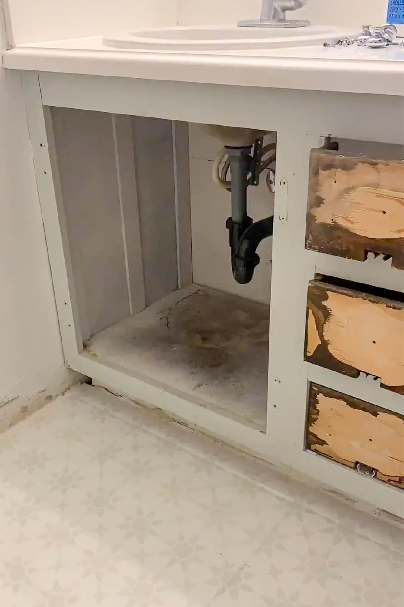 Vanity cabinet interior exposed with plumbing visible before painting