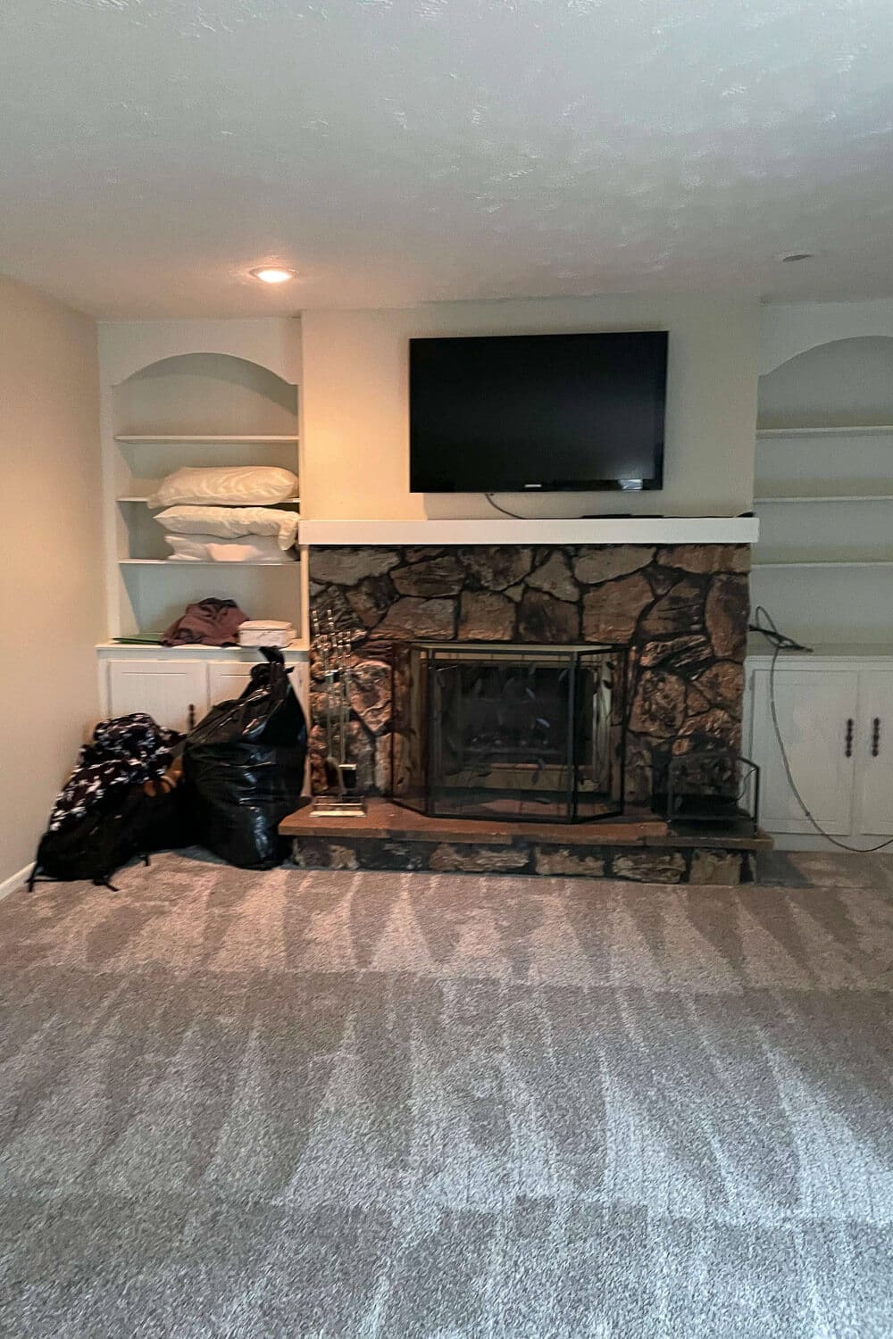 living room before remodel with dark rock fireplace, old built-ins, and beige walls