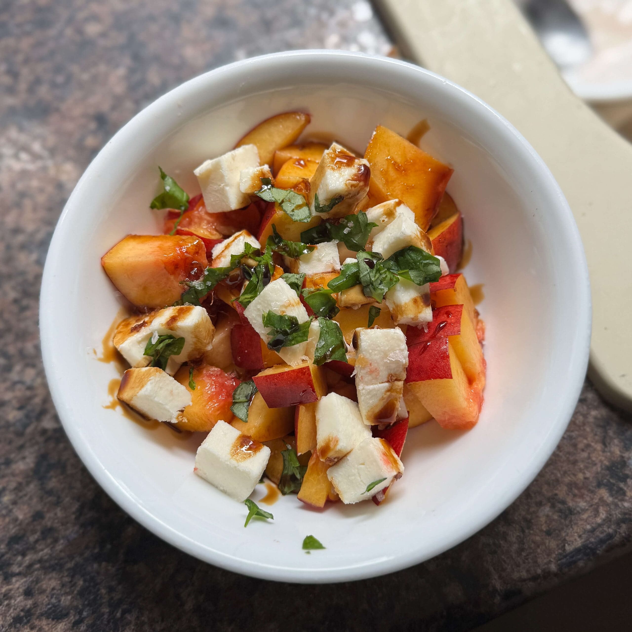 Nectarine salad with mozzarella and basil topped with balsamic glaze in a round white bowl, photographed from above.