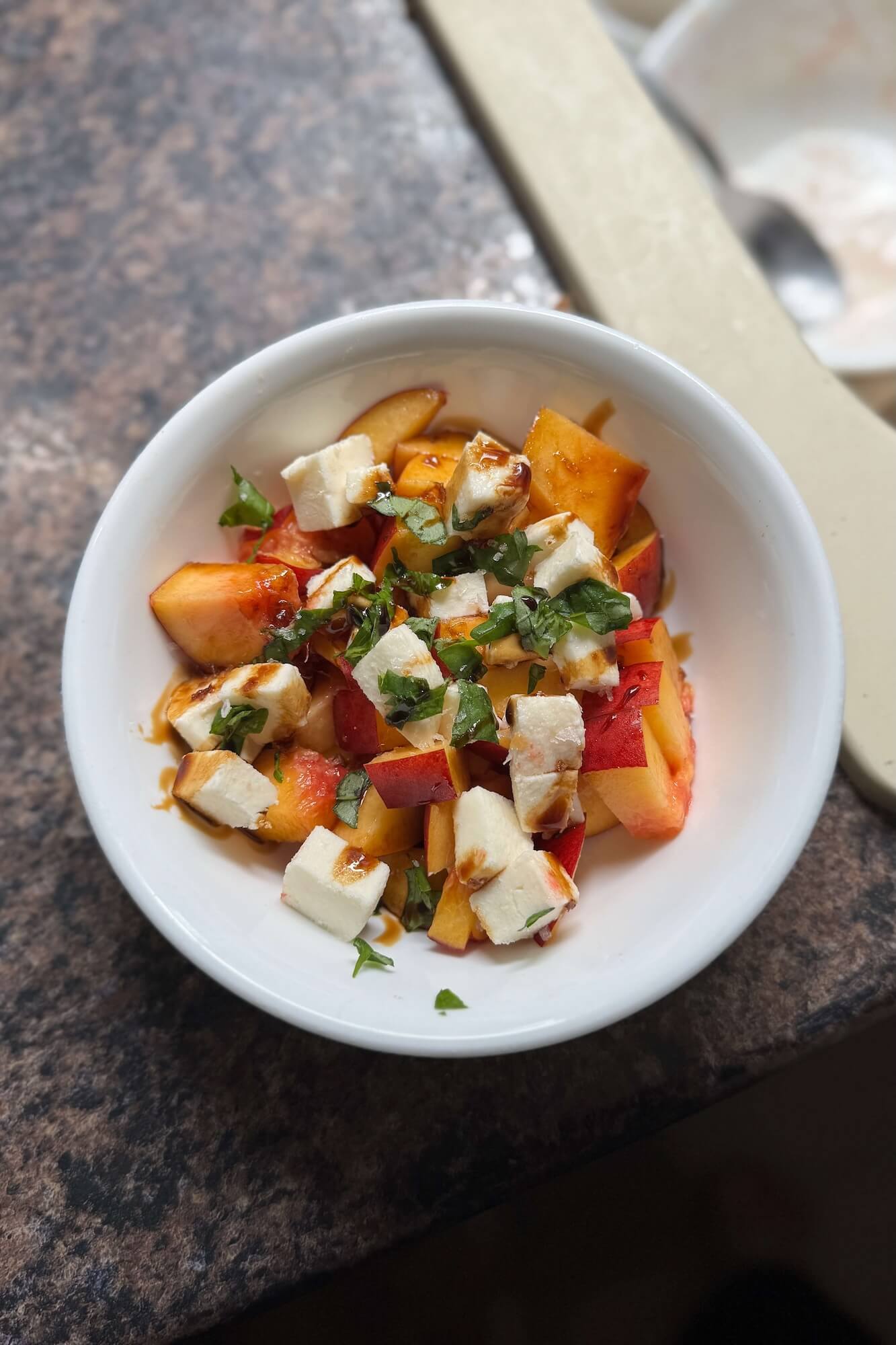 Nectarine salad with mozzarella and basil topped with balsamic glaze in a round white bowl, photographed from above.