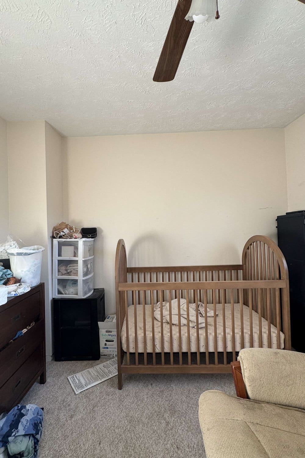 Nursery before makeover with cluttered corner, crib, and beige walls.