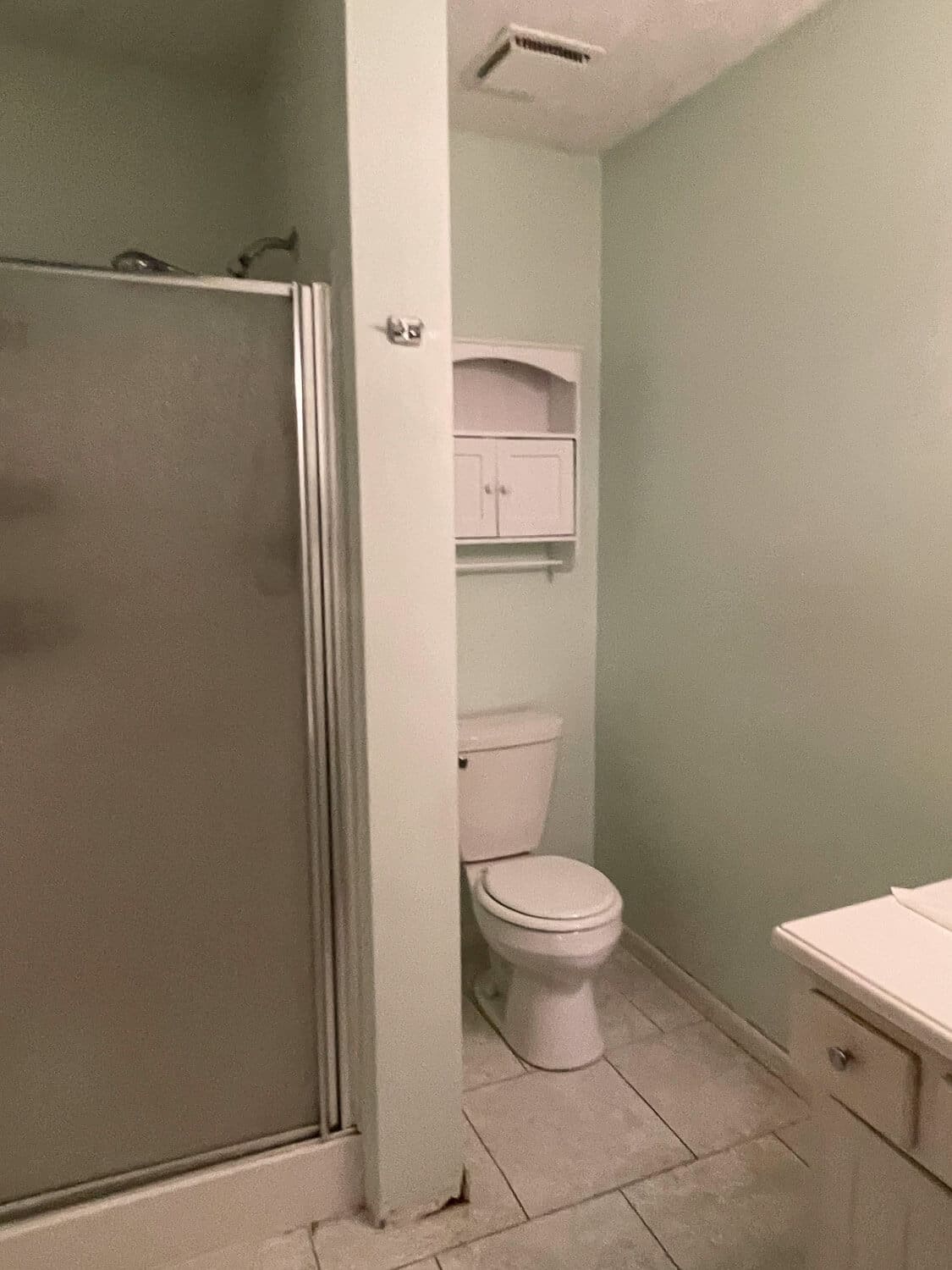 Outdated bathroom before remodel with green walls, corner shower, and old tile.