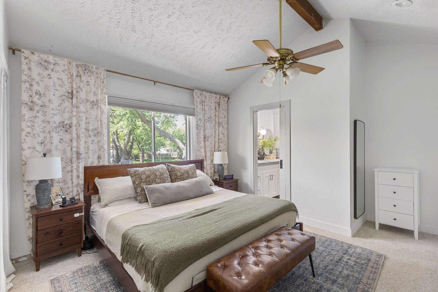 Cozy primary bedroom after DIY home renovation with neutral bedding and leather bench.
