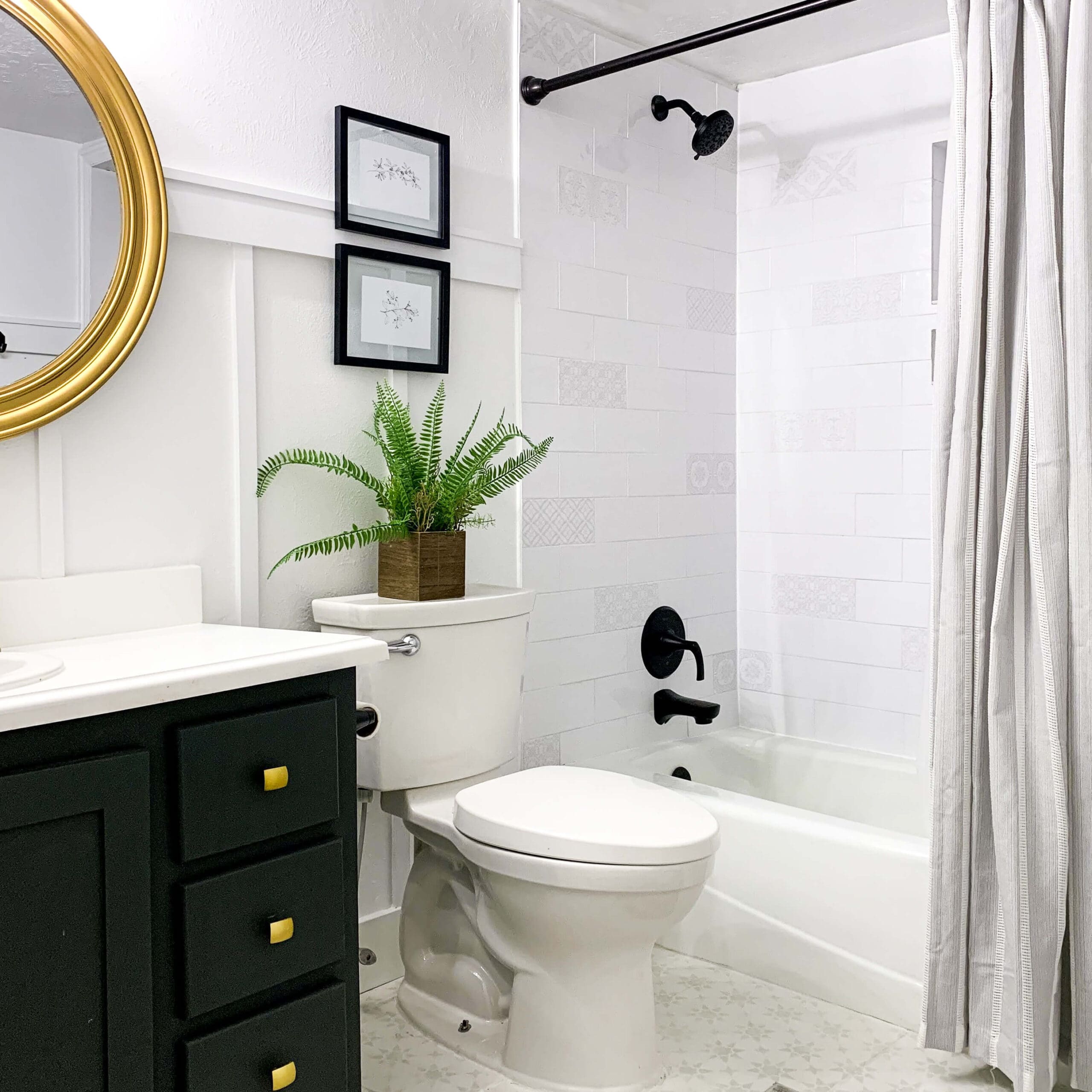 Stylish small bathroom makeover featuring green vanity, board and batten walls, black hardware, and tiled bathtub.