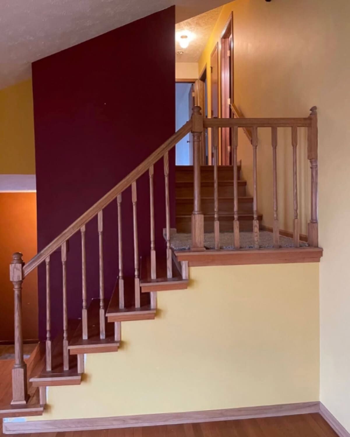 Staircase before DIY home renovation with yellow and red walls and oak railing.