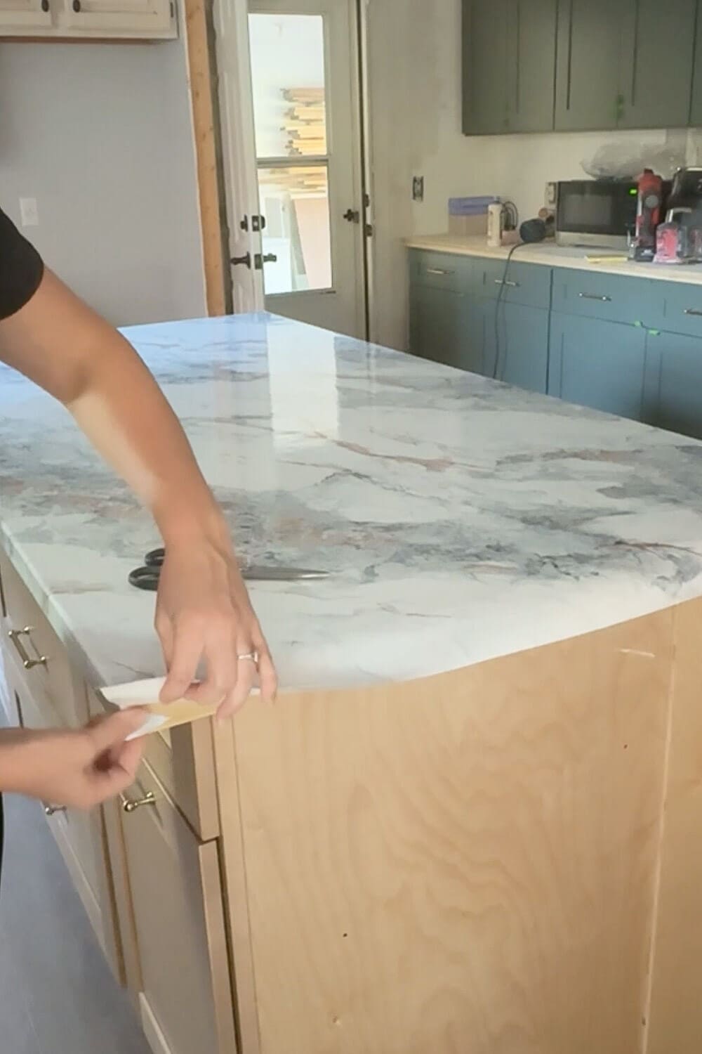 Wrapping marble contact paper around the edge of a kitchen island countertop, trimming for a clean finish in a DIY faux marble makeover.