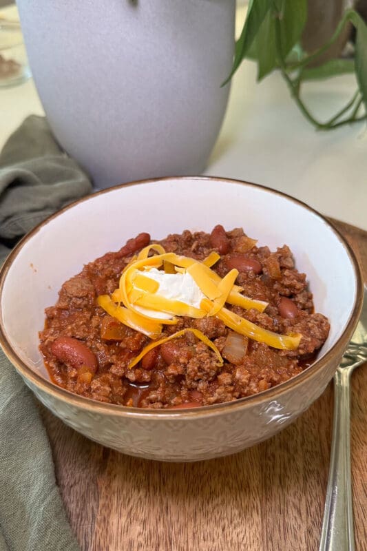 Hearty blue ribbon chili with ground beef and beans in a bowl, finished with shredded cheddar and a dollop of sour cream—classic cold-weather dinner.