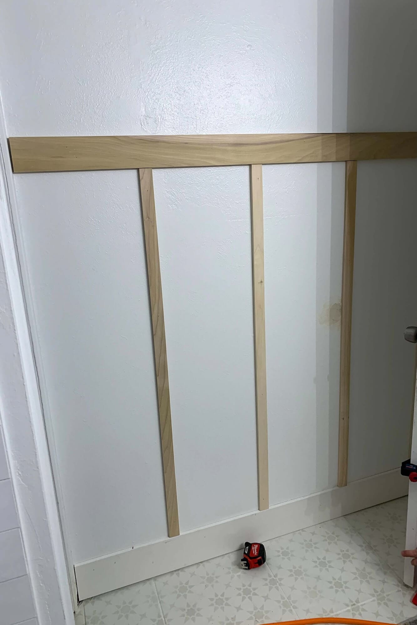 Early layout of a board and batten wall showing a 1x4 top board and measured 1x2 battens before caulk and paint.
