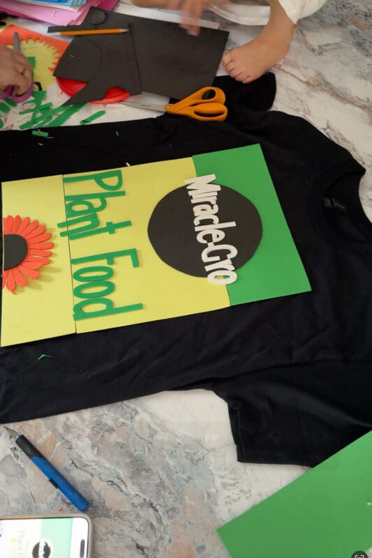 Completed DIY costume t-shirt design featuring colorful foam letters and a flower detail, a funny homemade Halloween idea for a garden theme, dressing as a bag of fertilizer, made with simple craft supplies.