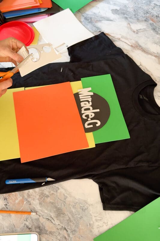 Hands cutting out white foam letters for a DIY costume t-shirt logo as part of a simple and funny Halloween shirt idea.