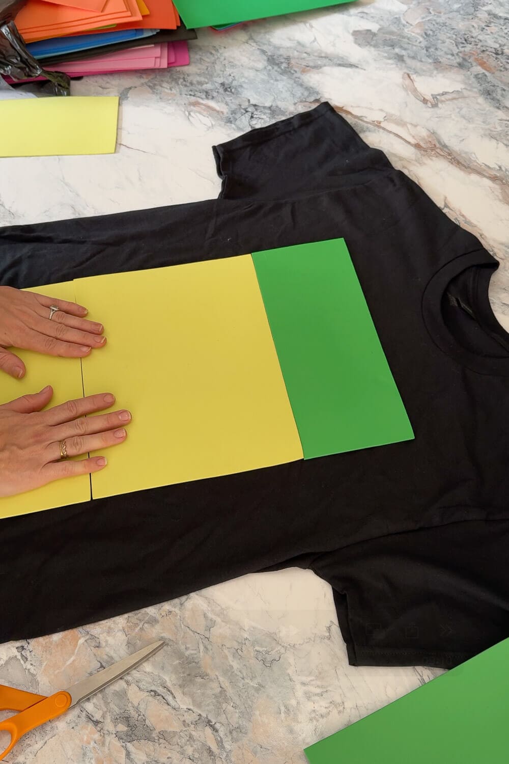 Hands laying decorations on a black shirt during a DIY craft project on a marble countertop.