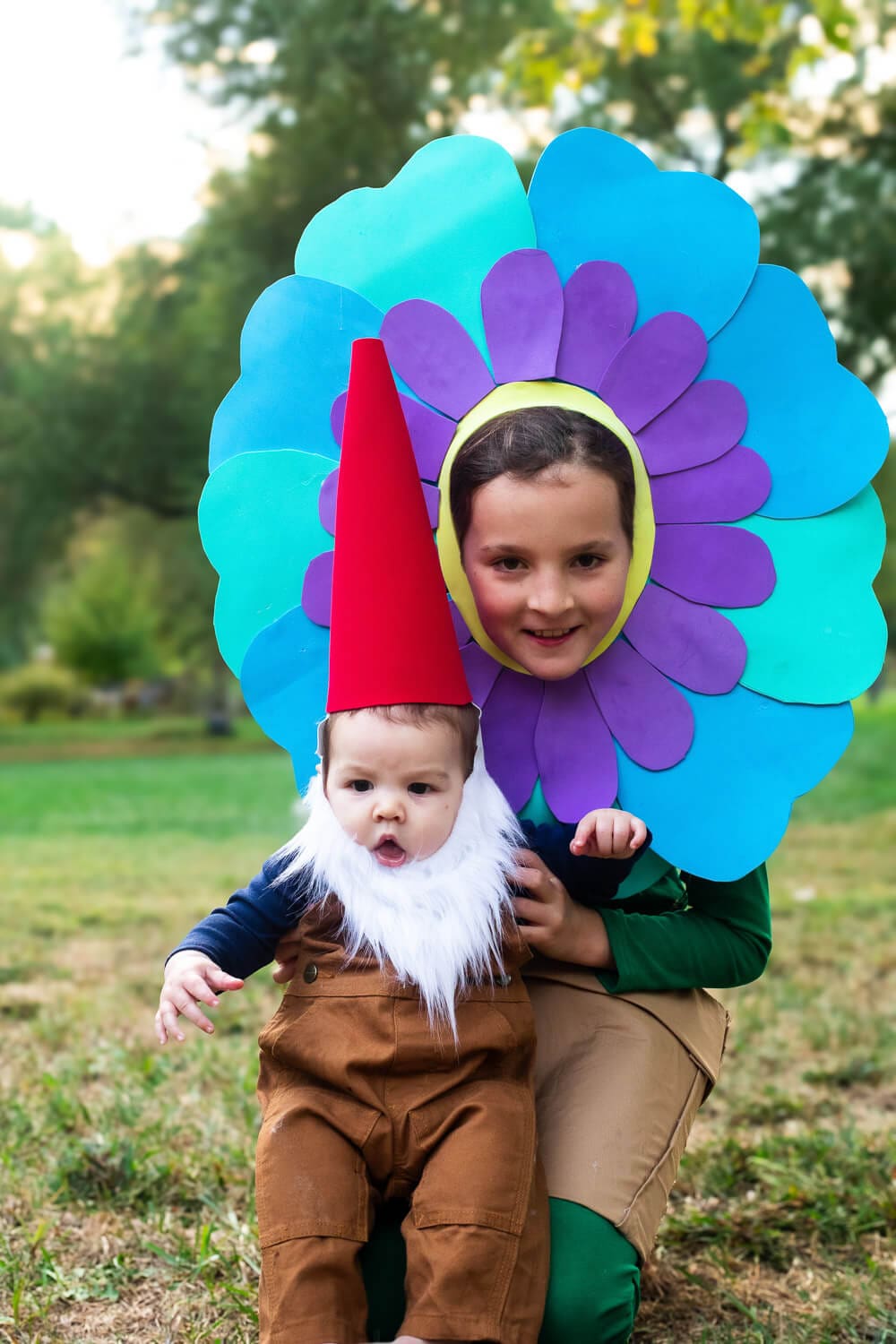 Older sister dressed as a flower for Halloween poses with her baby brother dressed as a garden gnome with a red hat and white beard