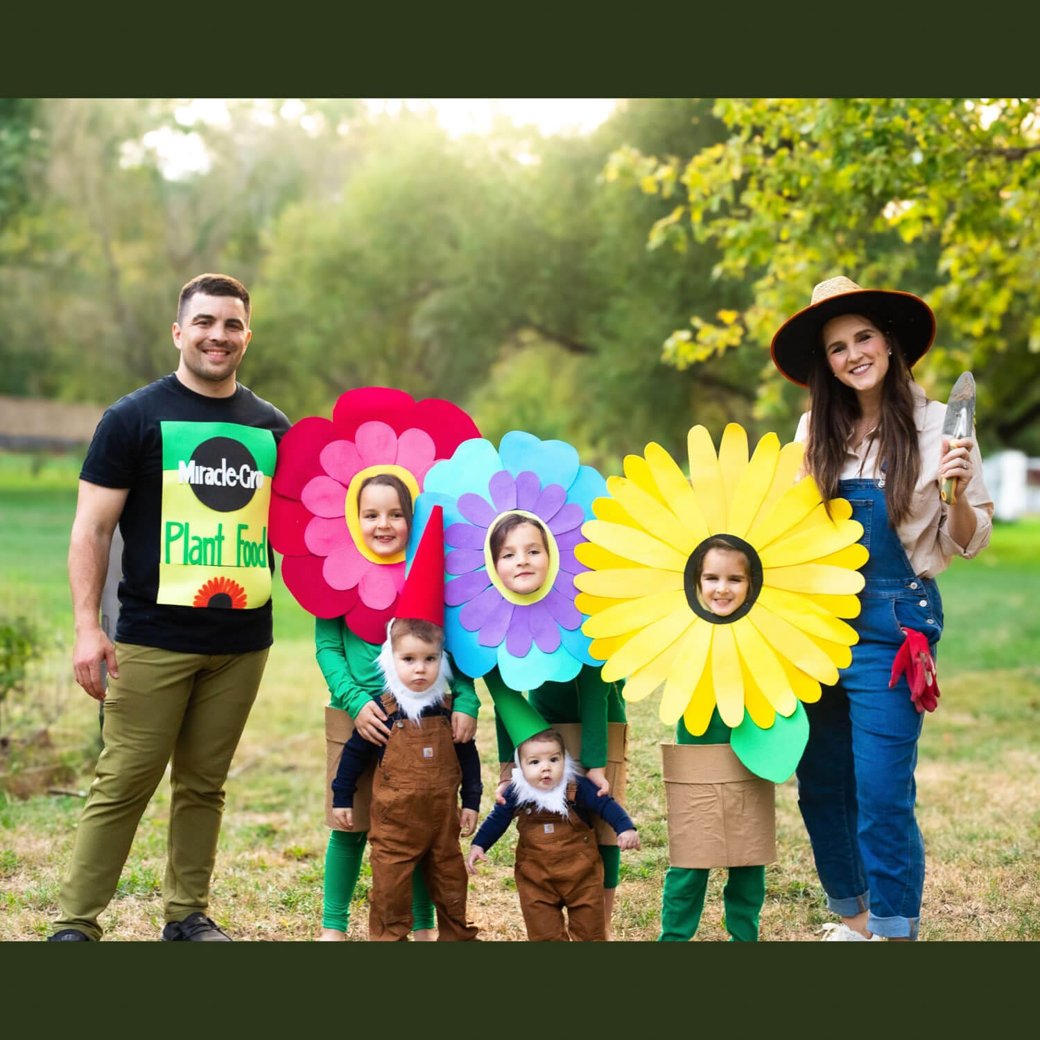 DIY family costume, garden theme: dad in Miracle-Gro plant food shirt, three kids as giant paper flowers, two toddlers as garden gnomes, and mom dressed as a gardener with a trowel.