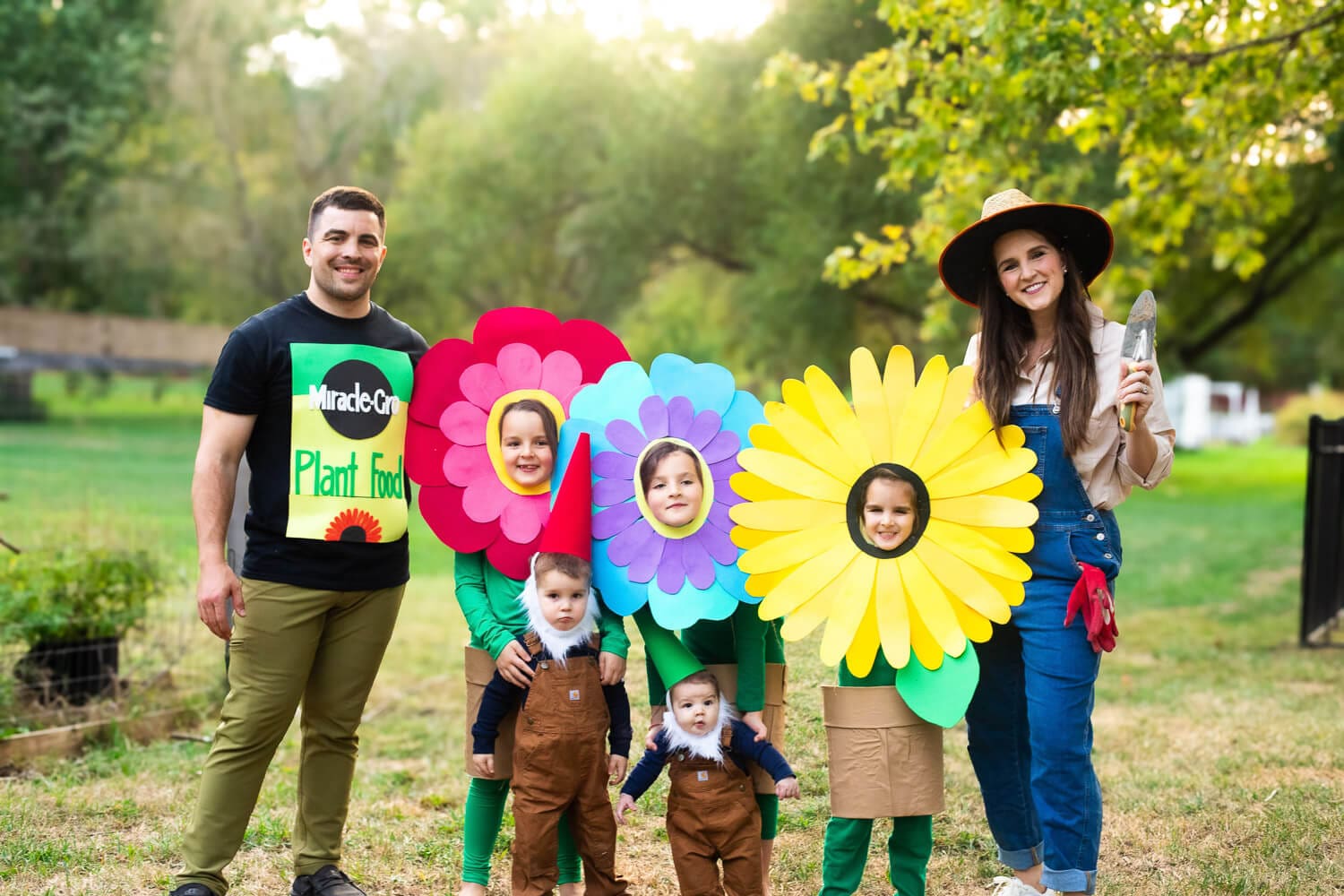 Garden-themed Halloween for big families: bright flower headpieces with pot skirts, toddler gnome hats and beards, dad in fertilizer T-shirt, and mom gardener in overalls.