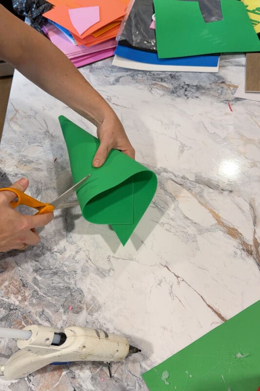 Trimming the tip of a green foam cone while shaping a no-sew gnome costume hat during an easy Halloween craft.