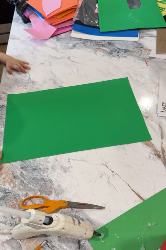 Green foam sheet laid flat on a marble counter before being rolled into a cone for a no-sew DIY gnome costume hat.