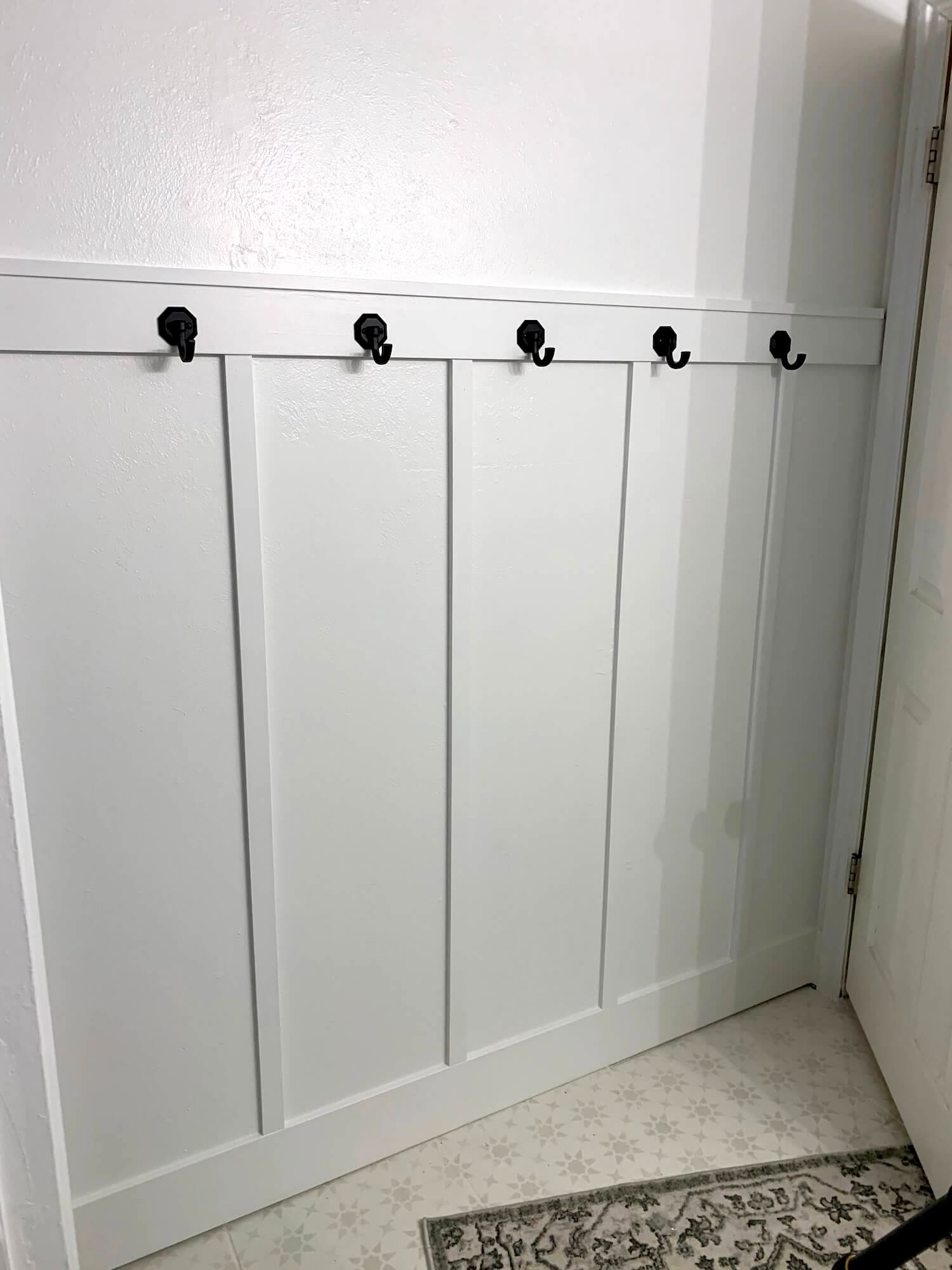 DIY board and batten bathroom wall painted white with black hooks along the top trim