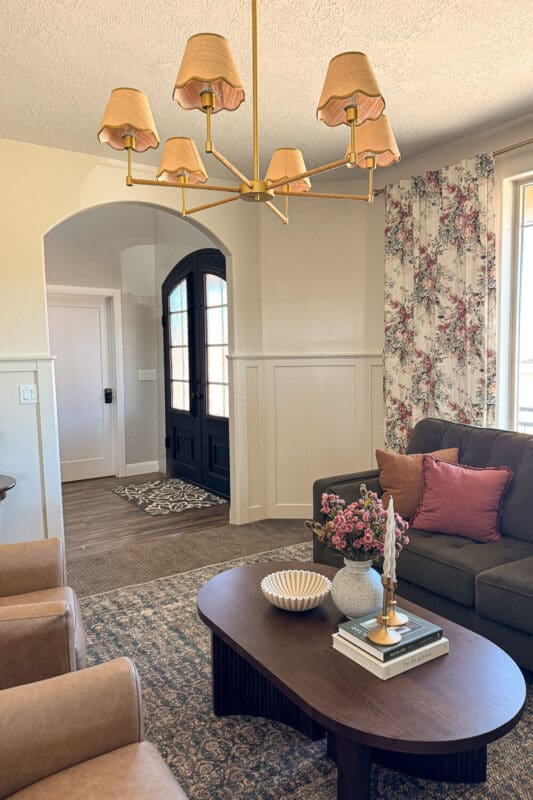 Formal living room after makeover with olive green sofa, floral curtains, brass chandelier, styled coffee table, and warm neutral walls.