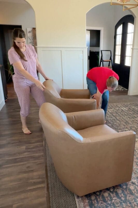 Positioning two tan leather armchairs on the rug to create a conversation layout in a formal living room with board and batten walls.