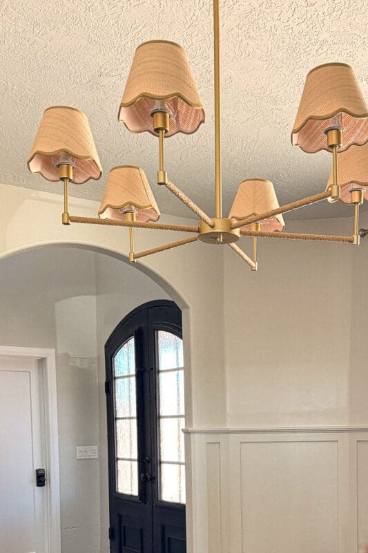 Close-up of brass chandelier with scalloped fabric shades in a formal living room with Accessible Beige walls, board and batten, arched doorway, and black double doors.